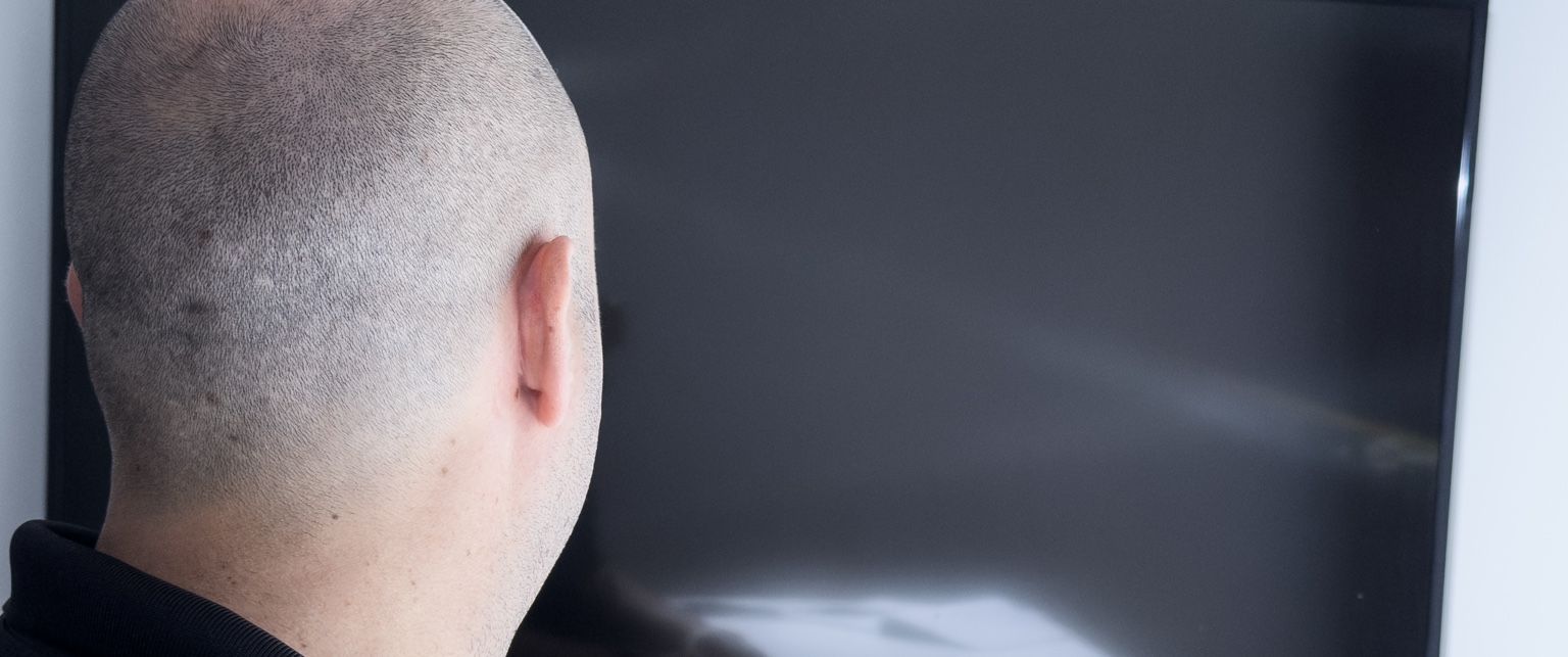 The back of a man’s head as he watches a television in a living room.