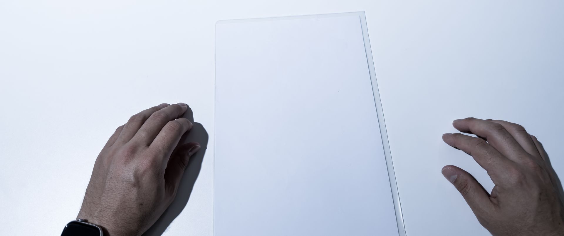 Two hands holding a blank white card against a white table.