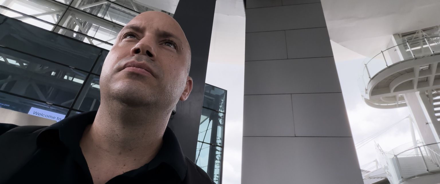 A man looking up from a low angle under a curved glass roof.